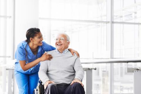 Hospital worker in blue scrubs stood next to elderly man in wheelchair