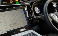 Car dashboard and steering wheel with a laptop next to them displaying data captured from the car.